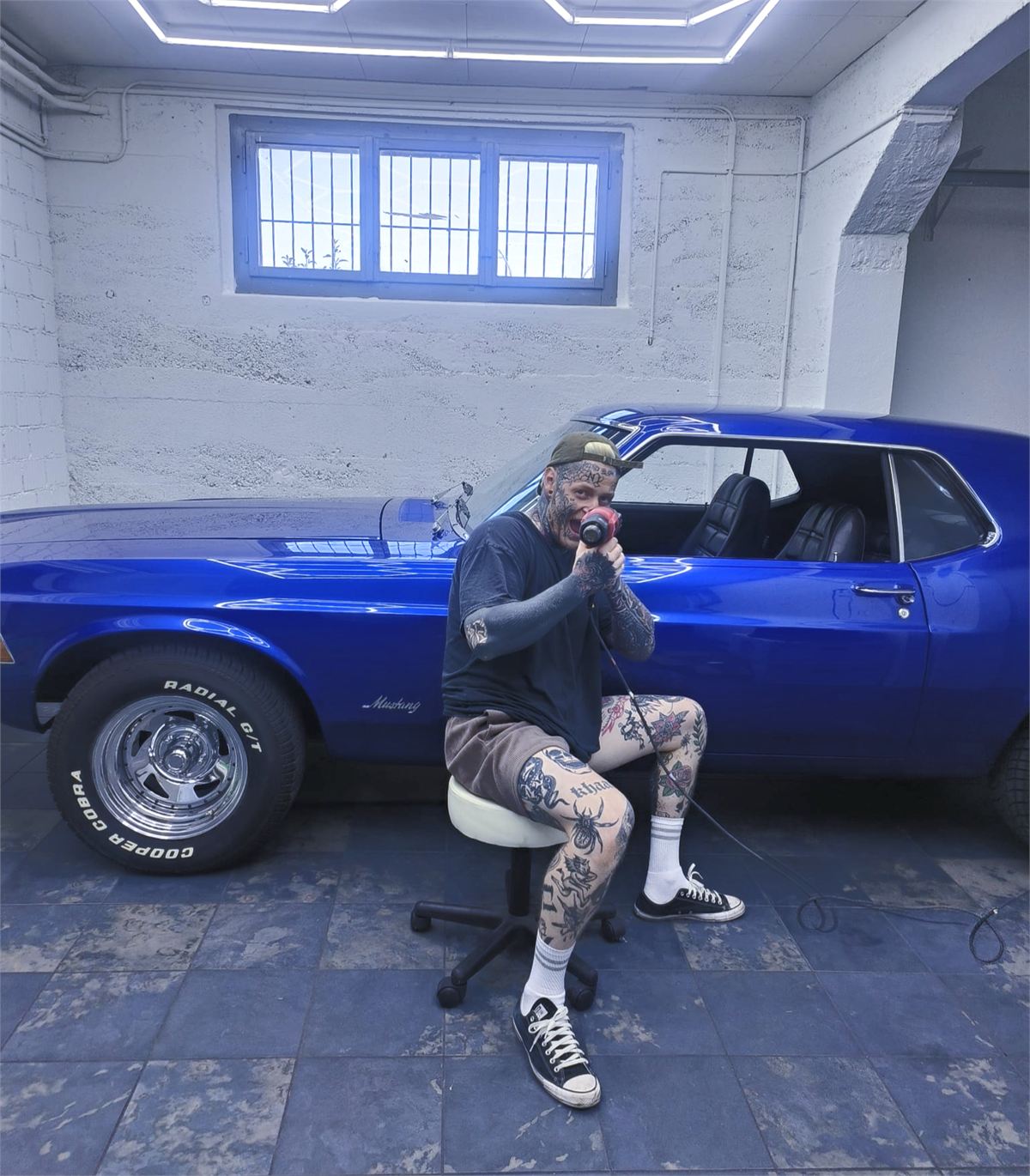 Nic sitzt mit dem Heissluftföhn in der Hand vor einem blau folierten Ford Mustang in seiner Werkstatt
